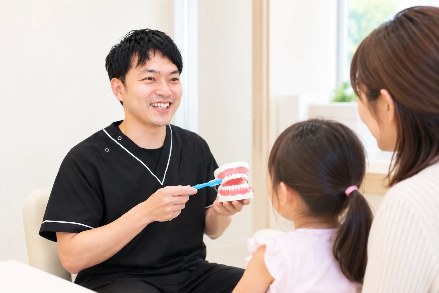 歯の模型と歯ブラシで、お子さまと保護者に歯みがきを説明する歯科医師